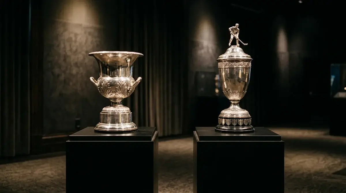 NHL Conn Smythe and Vezina trophies displayed on plinths under stadium spotlights